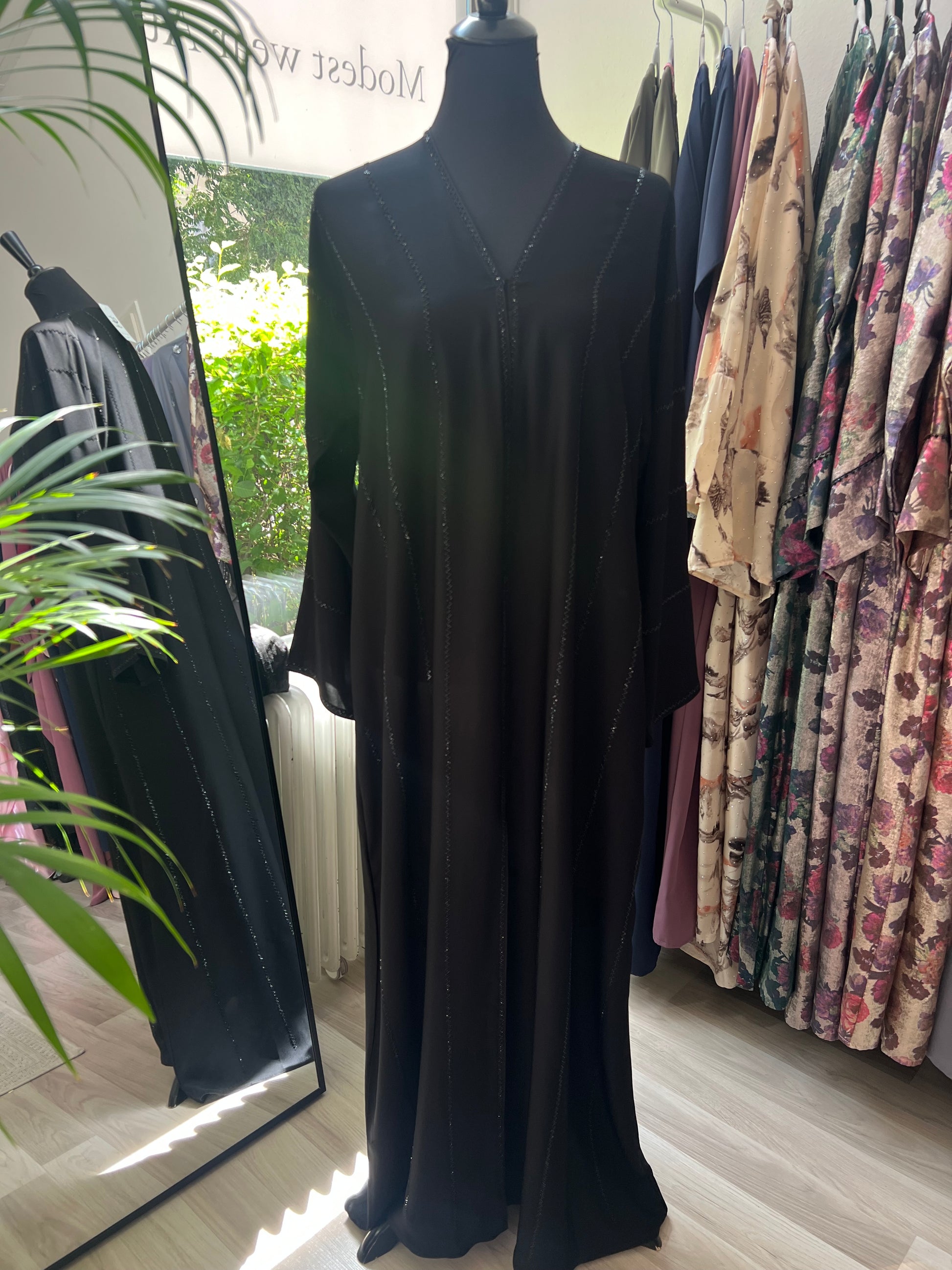 Vollansicht-der-schwarzen-Abaya-Salma auf-einer-Puppe-mit-zarten-Glitzerlinien,-fotografiert-im-Tageslicht-im-Sheylin Showroom.