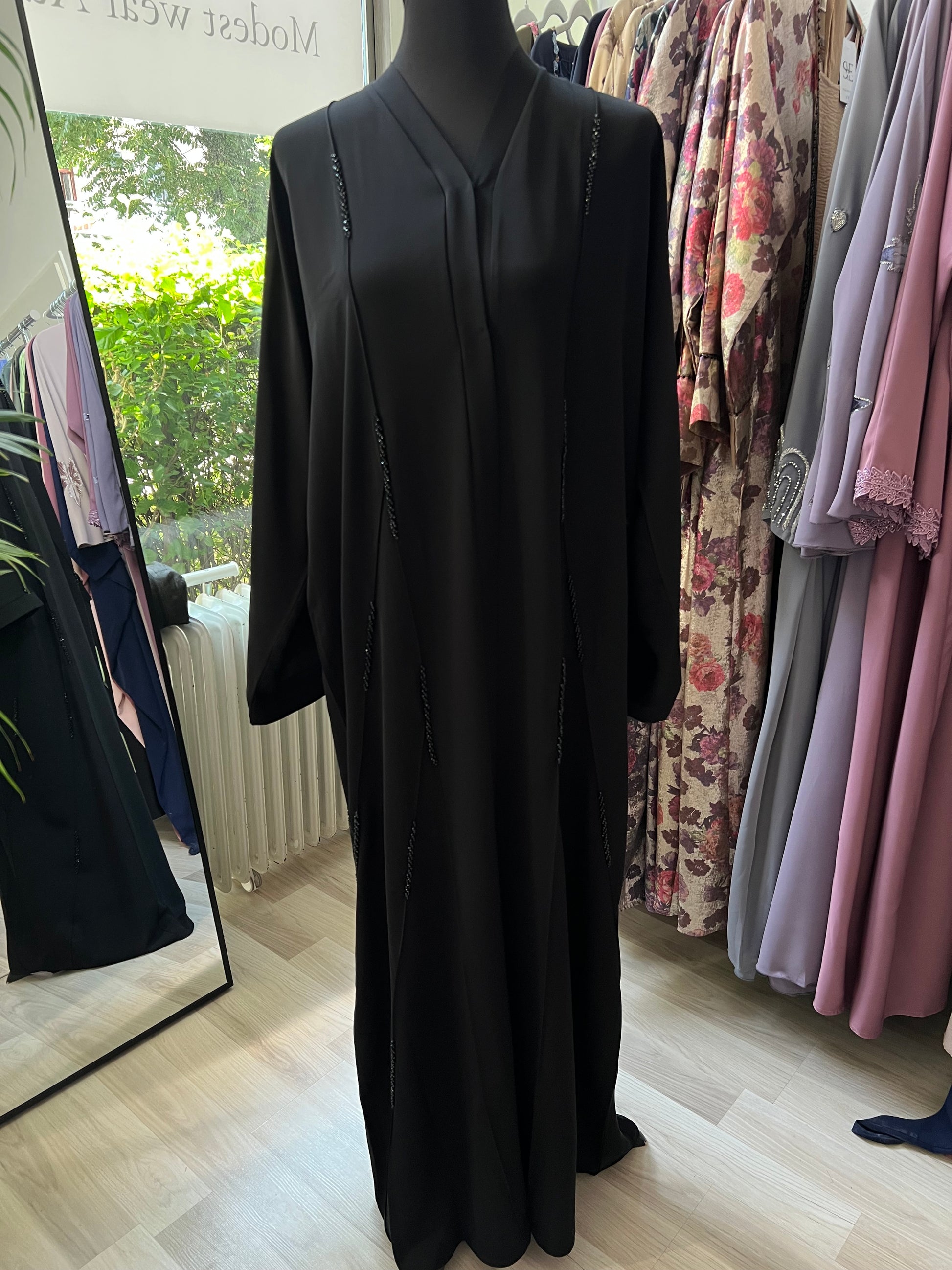 Vollansicht der Abaya Zahra in Schwarz mit feiner Perlenverzierung entlang der Vorderseite – aufgenommen im Sheylin Showroom.