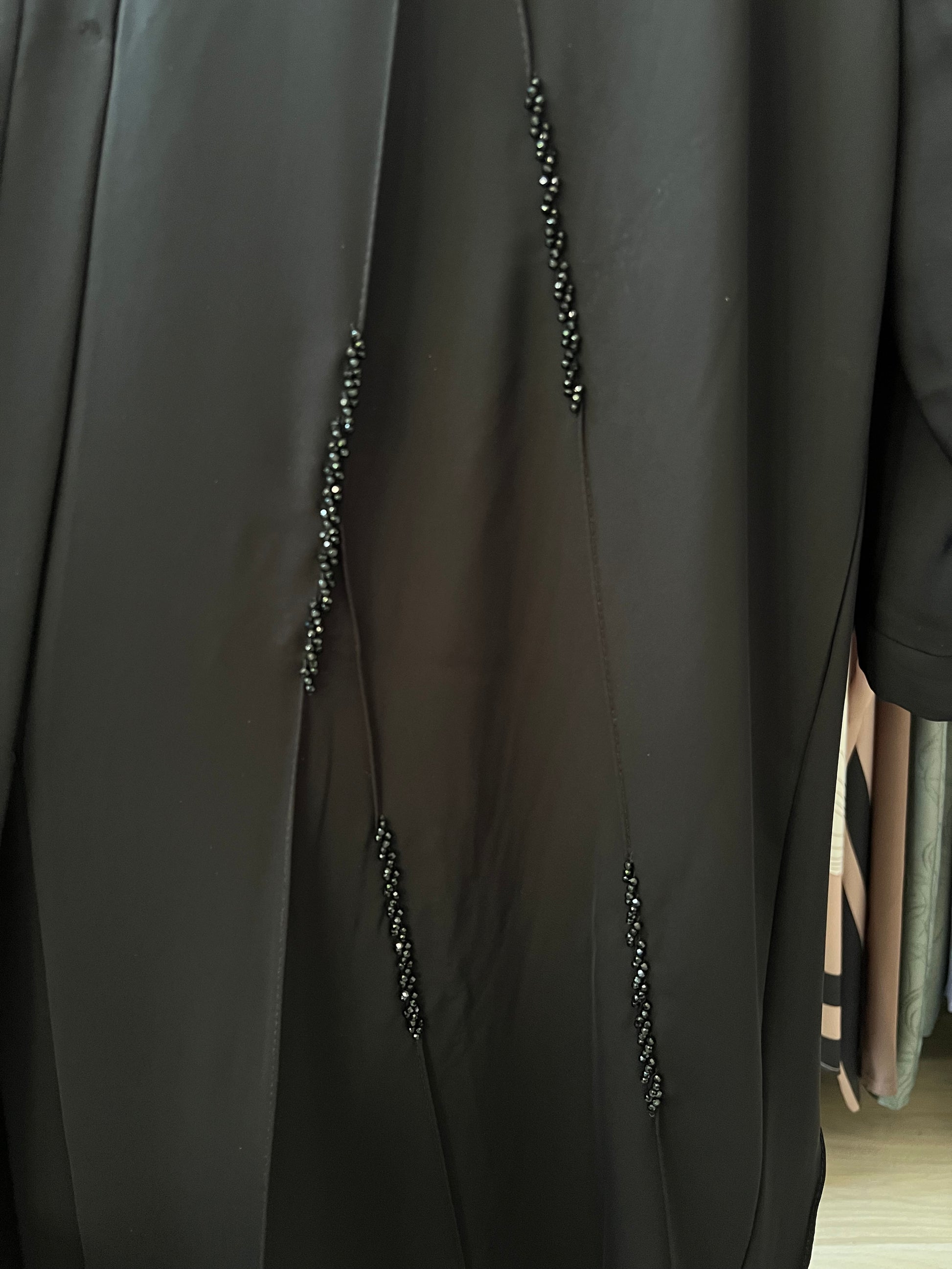 Detailaufnahme der schwarzen Perlenstickerei in vertikaler Anordnung auf dem Stoff der Abaya Zahra.