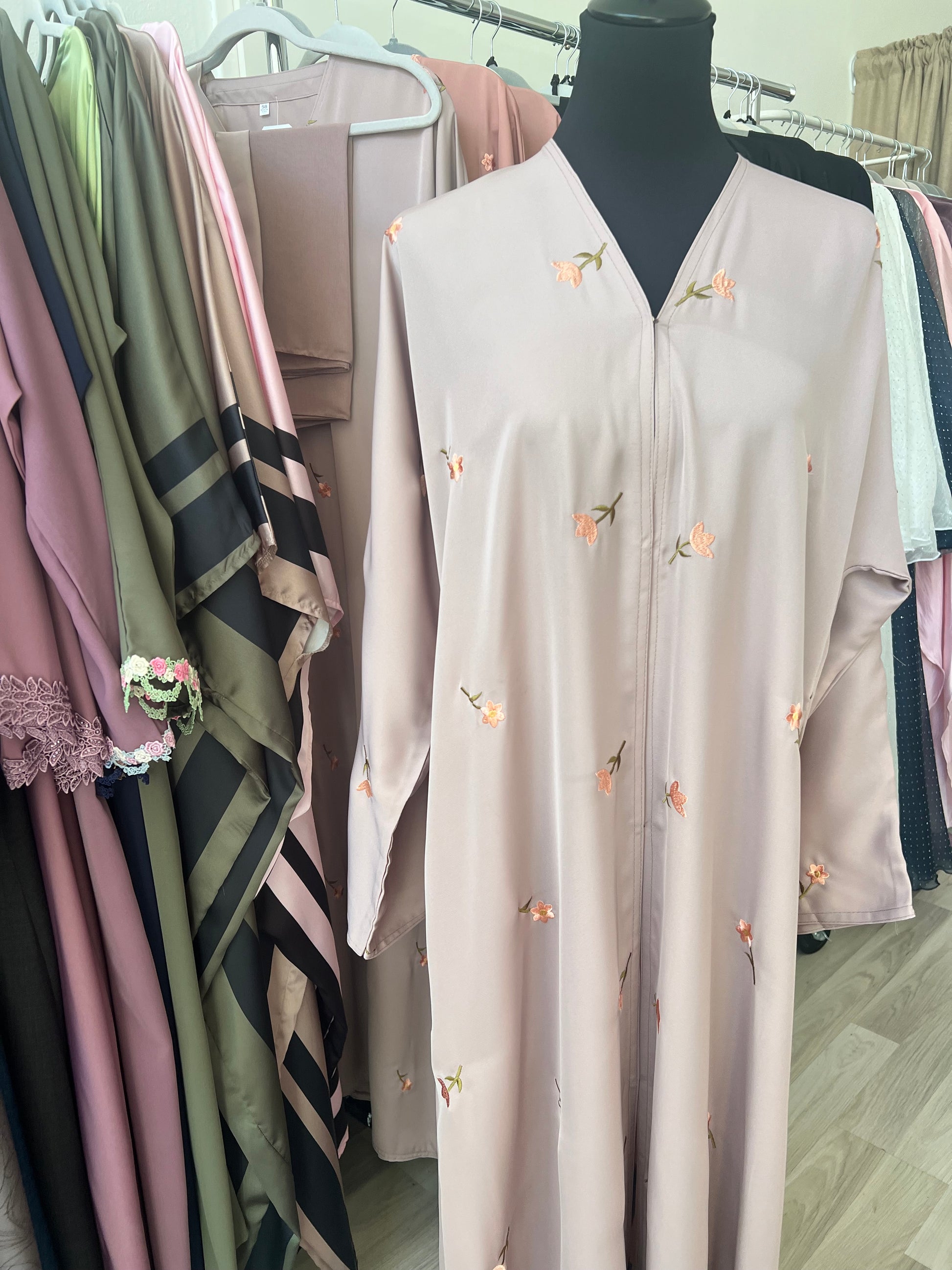 Nahaufnahme der Abaya mit filigraner Blumenstickerei in Rosa und Grün – ausgestellt zwischen weiteren Modellen im Showroom.
