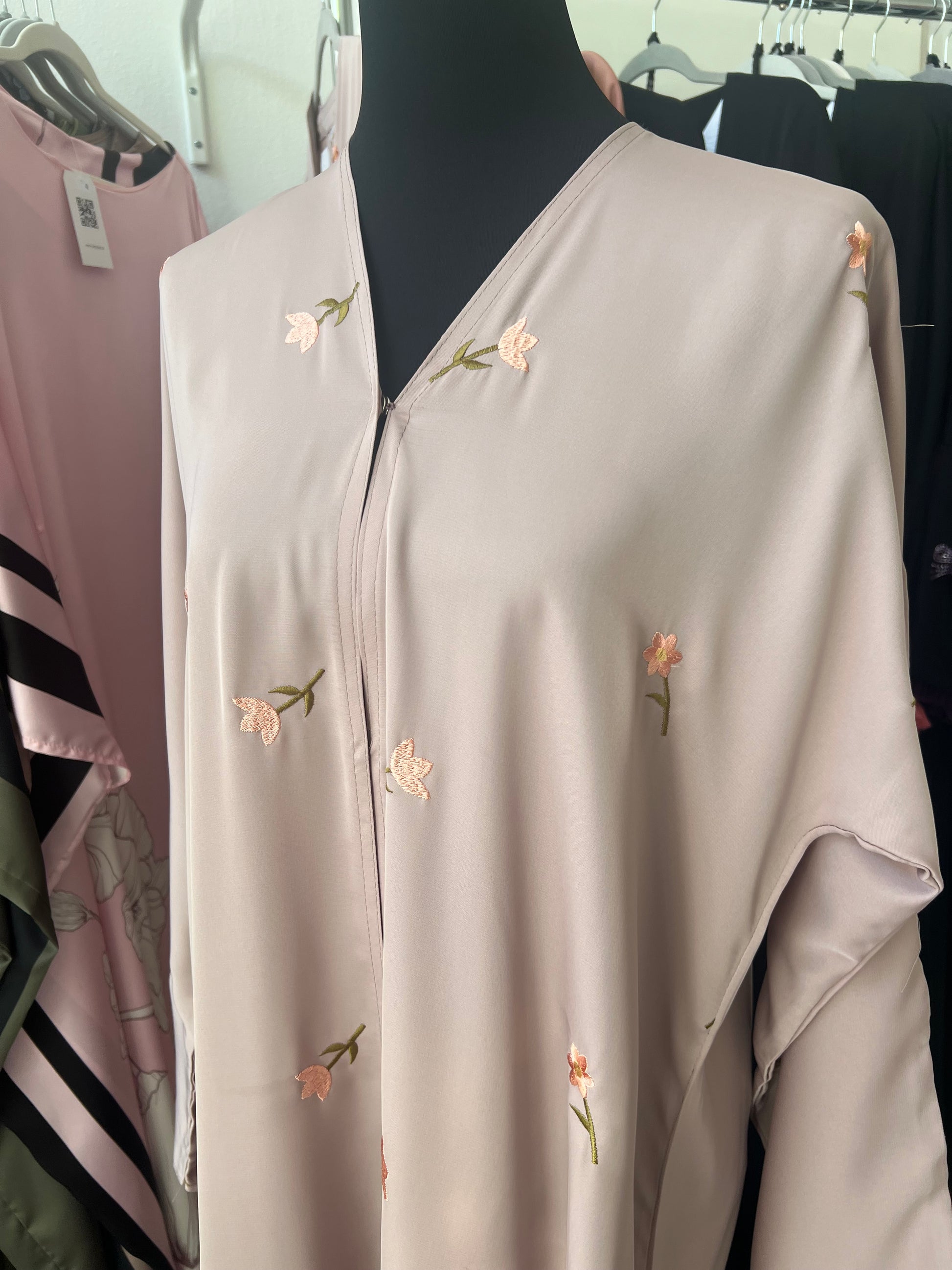 Detailansicht des oberen Teils der Abaya: feine Blütenstickereien auf fließendem, rosigem Stoff mit V-Ausschnitt.