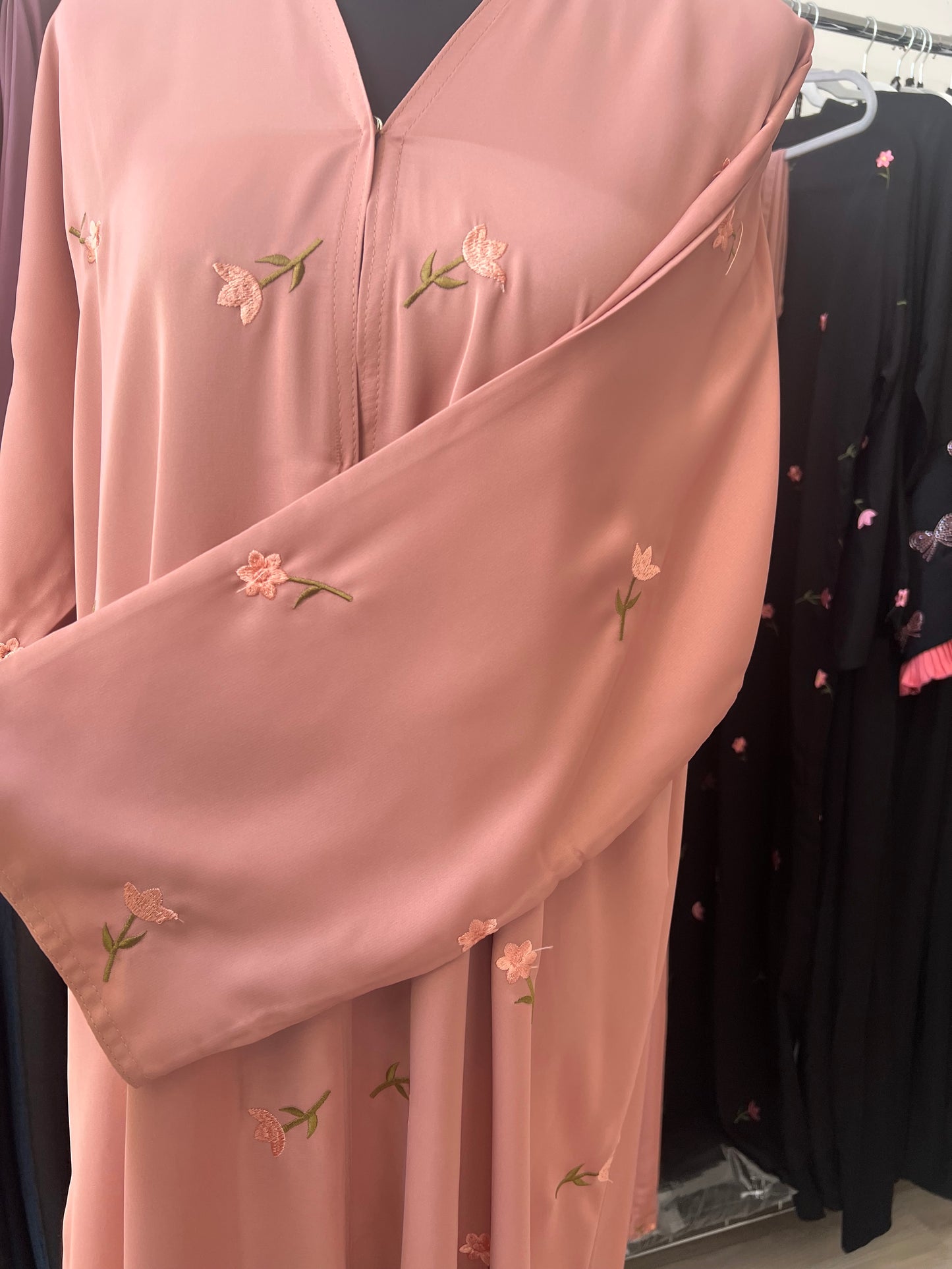Nahaufnahme des Ärmels der pfirsichfarbenen Abaya, über die Brust gelegt – mit gut sichtbarer, hochwertiger Blumenstickerei.