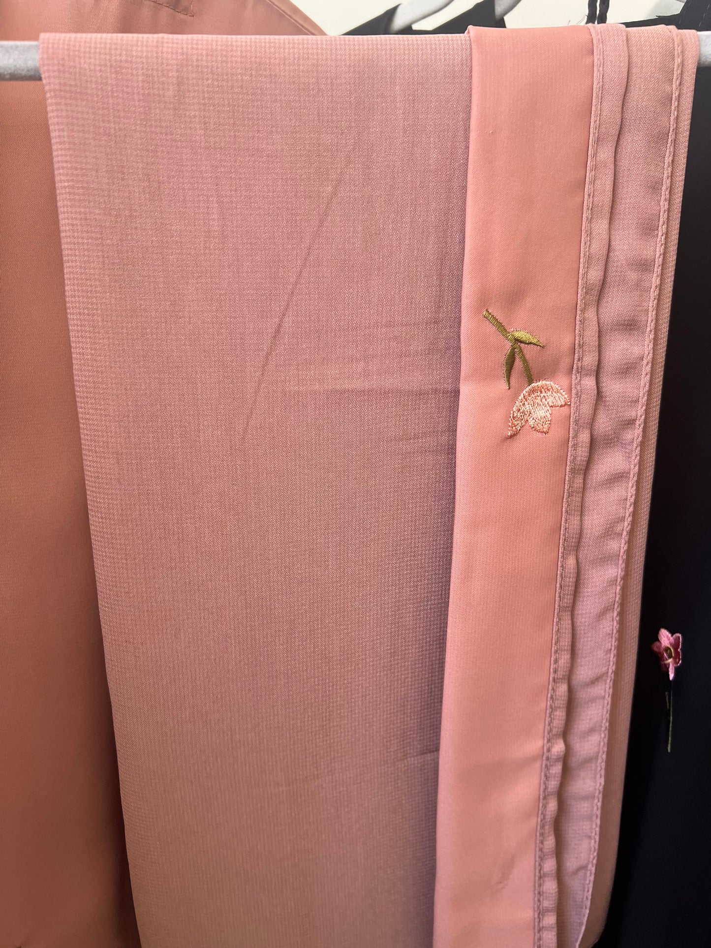 Passender pfirsichfarbener Hijab zur Abaya, sorgfältig gefaltet, mit gesticktem Blümchenmotiv am Rand.