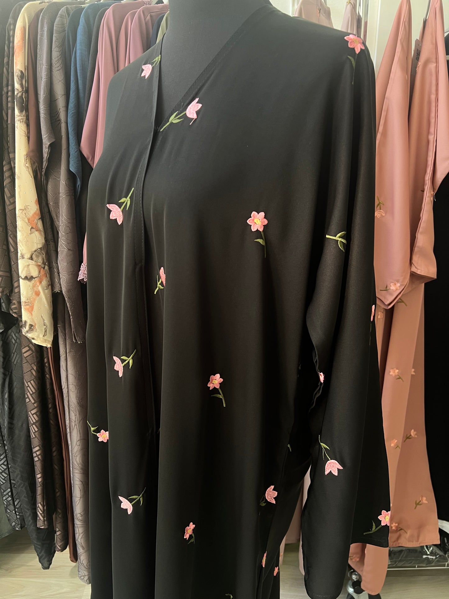 Seitliche Nahaufnahme der schwarzen Abaya mit zarten Blütenstickereien in Rosa – die Stickdetails heben sich edel vom dunklen Stoff ab.