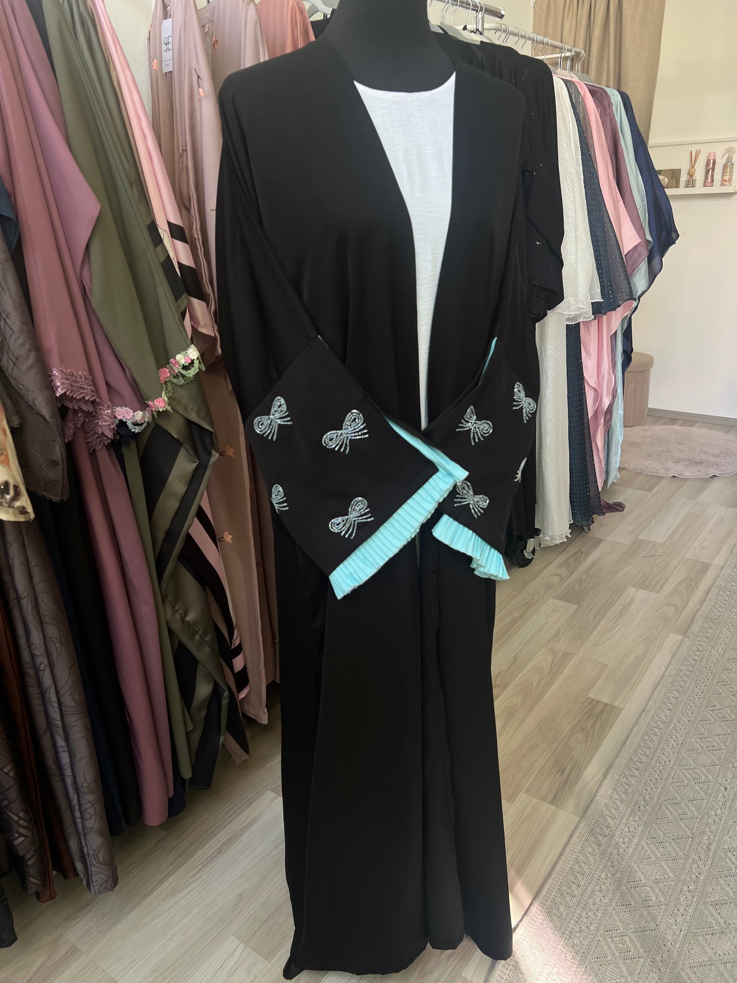 Nahaufnahme der Ärmel des Kimonos mit funkelnder weißer Schleifenstickerei und türkisfarbener Rüschenkante als verspielter Akzent.