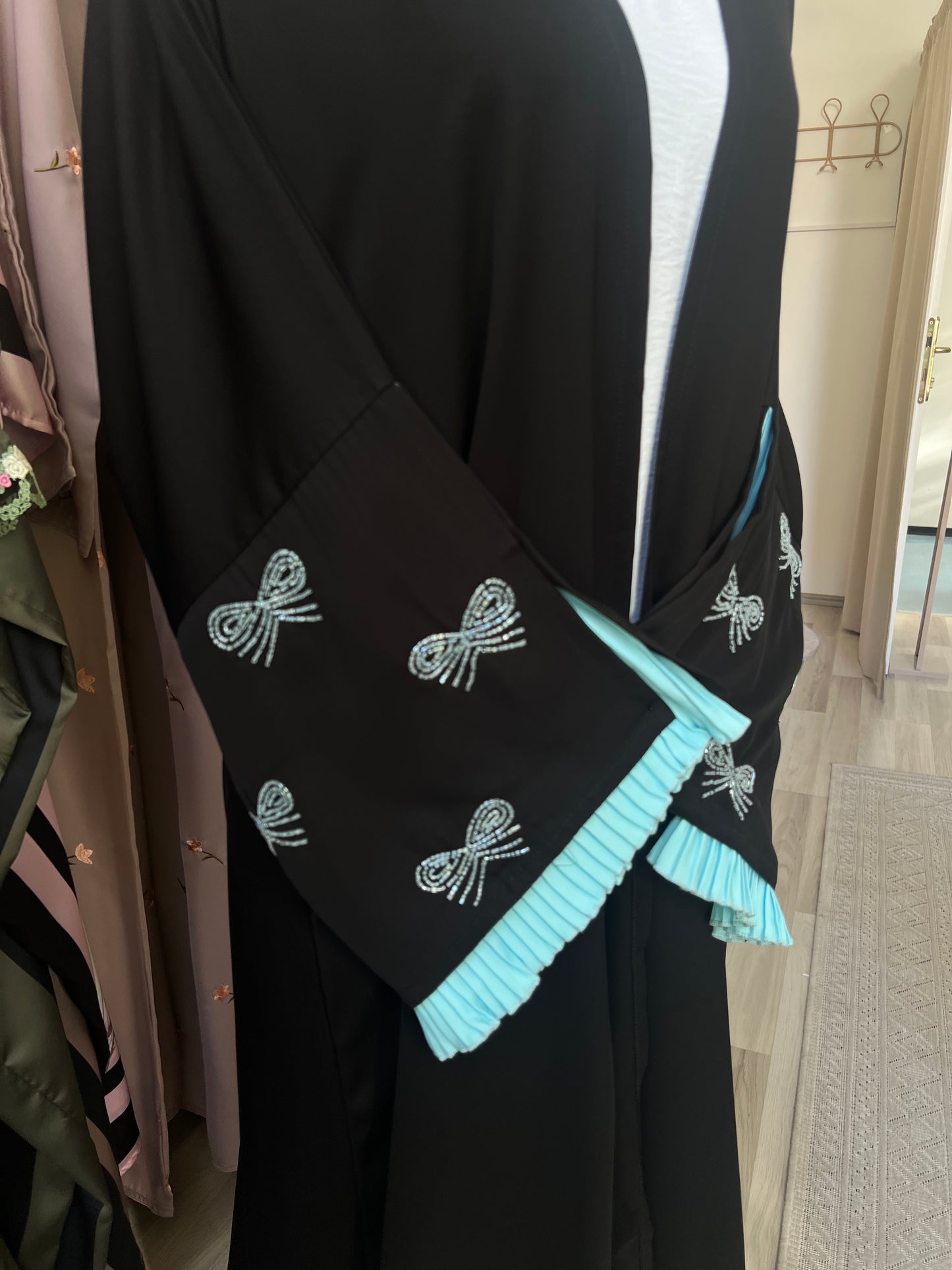 Detailansicht des schwarzen Kimonos mit elegantem Fall und bestickten Ärmeln – betont durch türkisfarbene Plisseerüschen und Schleifenmotive.