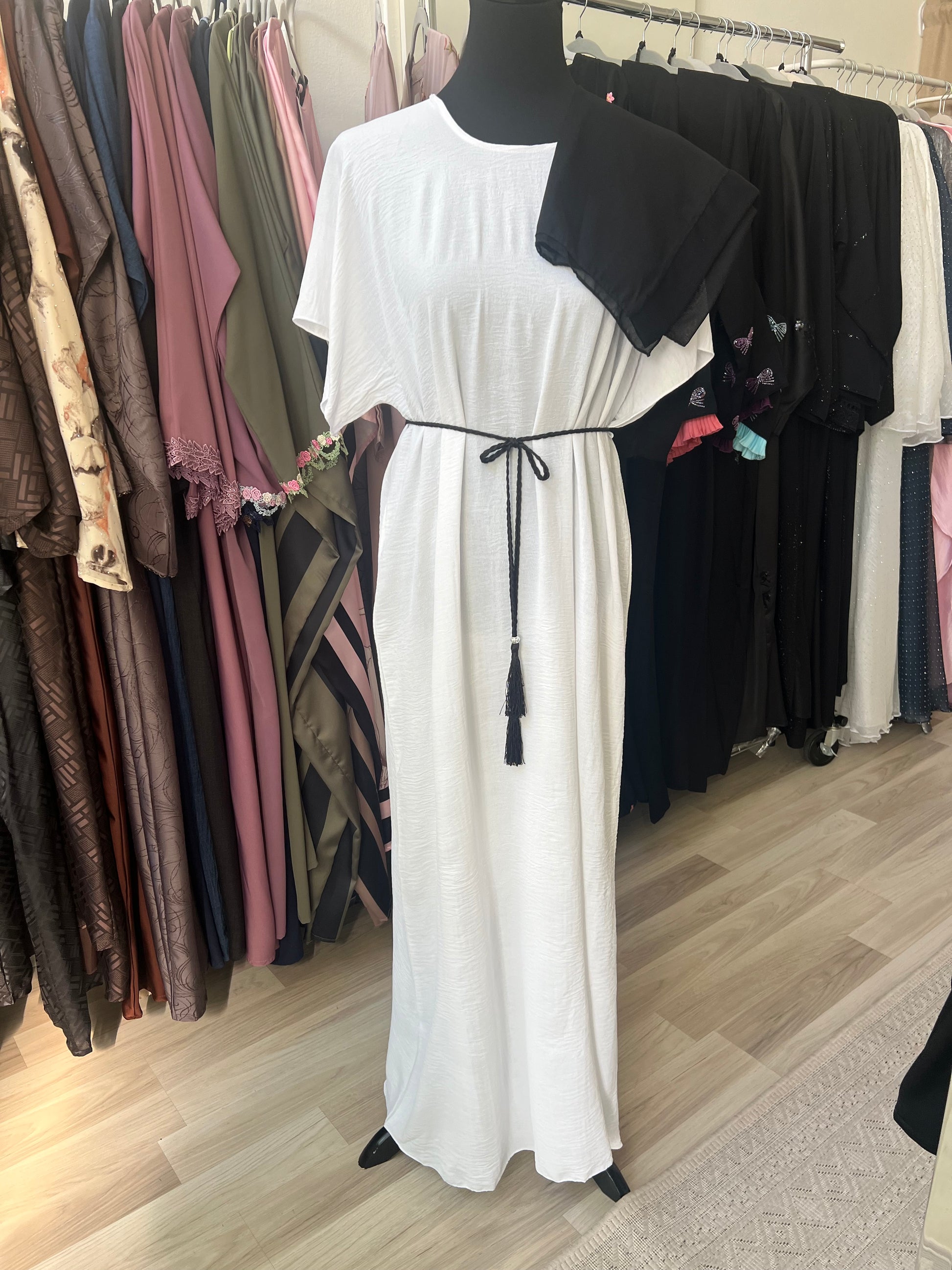Weißes Unterkleid mit schwarzem Kordelgürtel und schwarzem Hijab über die Schulter gelegt – das komplette Set der Abaya bestehend aus Kimono, Kleid und Hijab.
