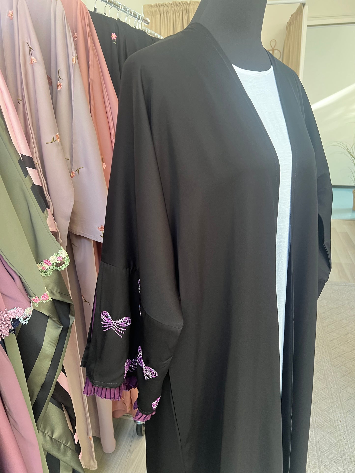 Seitenansicht der Abaya mit Fokus auf die violett plissierten Ärmelabschlüsse und funkelnder Schleifenstickerei in Lila und Silber.