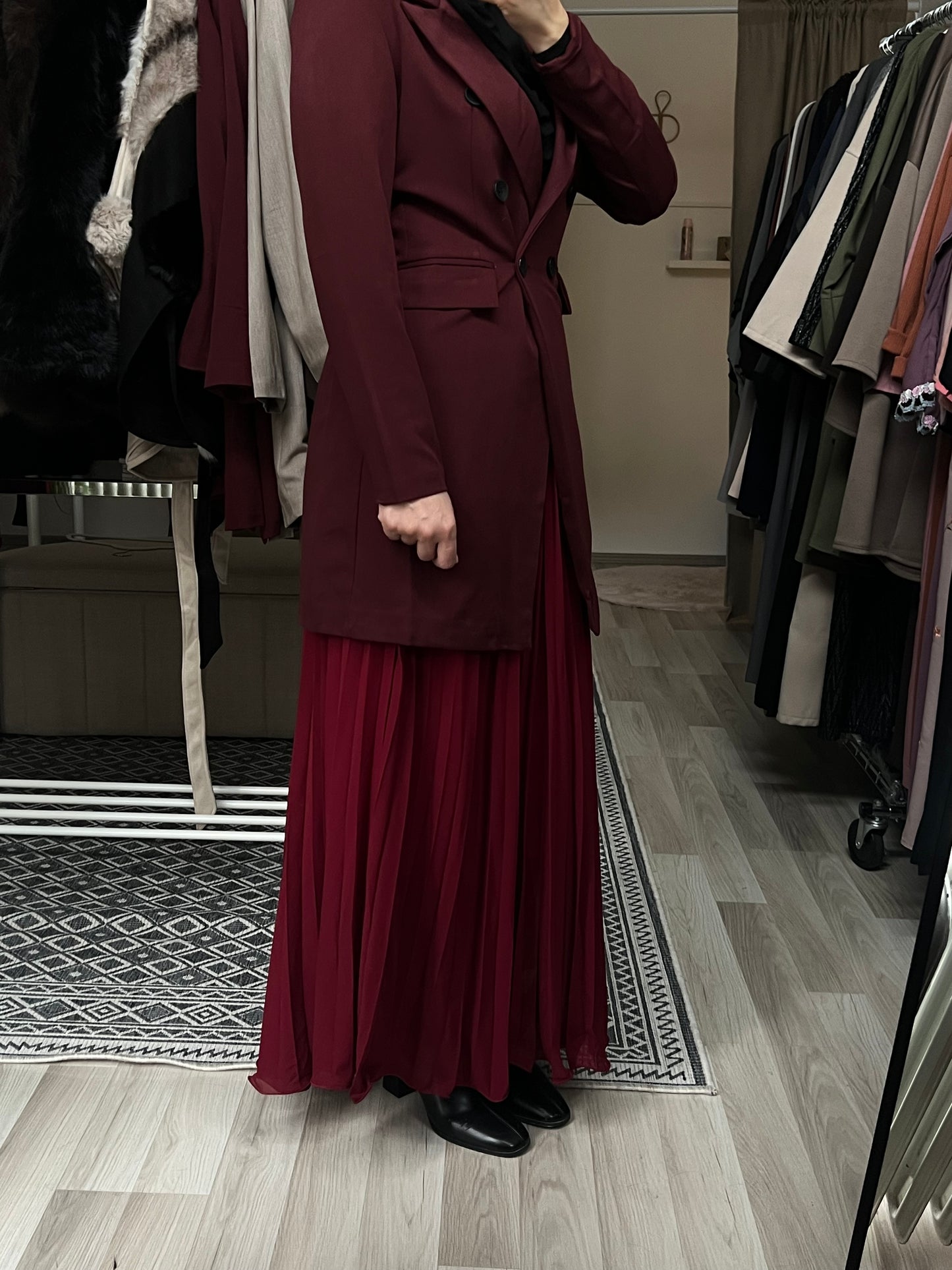 Seitenansicht eines bordeauxfarbenen Longblazers in eleganter, modester Passform mit tailliertem Schnitt, kombiniert mit passendem Plisseerock und schwarzem Hijab