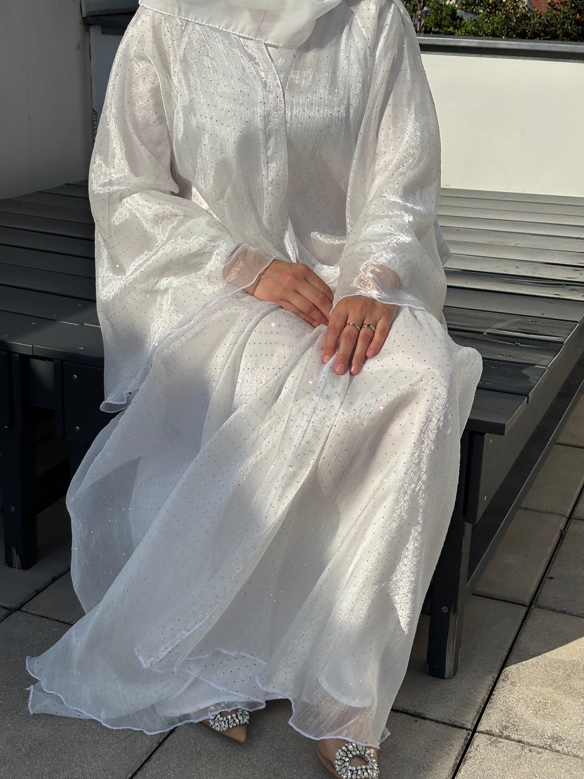 Sitzende Pose – Abaya Sheyla in Weiß mit funkelndem Fall, kombiniert mit Glitzerheels
