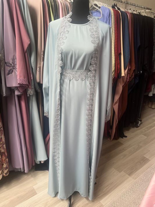 Hellblaue Abaya mit aufwendiger floraler Spitzenverzierung, komplettem Set auf Schneiderpuppe vor pastellfarbenem Hintergrund.