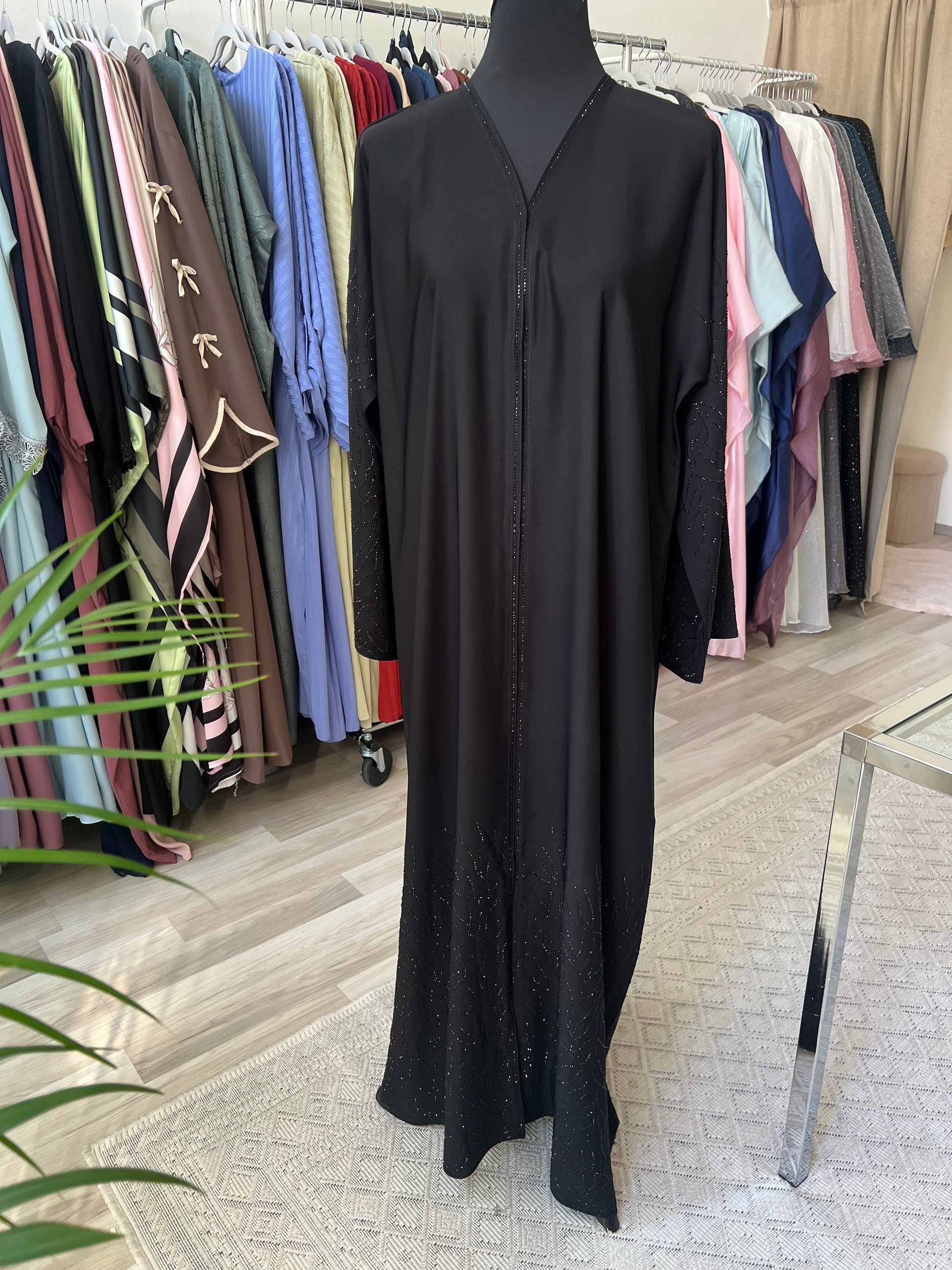 Vollansicht der schwarzen Abaya Noura auf einer Schneiderpuppe mit Glitzerverzierung an Ärmeln und Saum, aufgenommen im Sheylin Showroom.