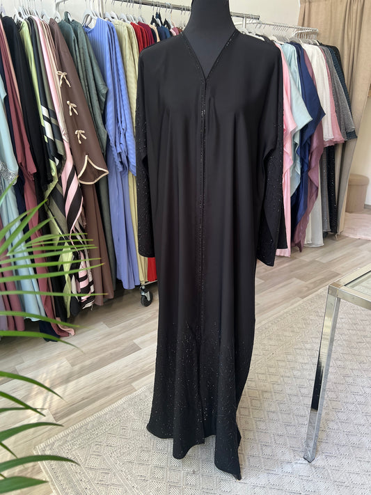 Vollansicht der schwarzen Abaya Noura auf einer Schneiderpuppe mit Glitzerverzierung an Ärmeln und Saum, aufgenommen im Sheylin Showroom.