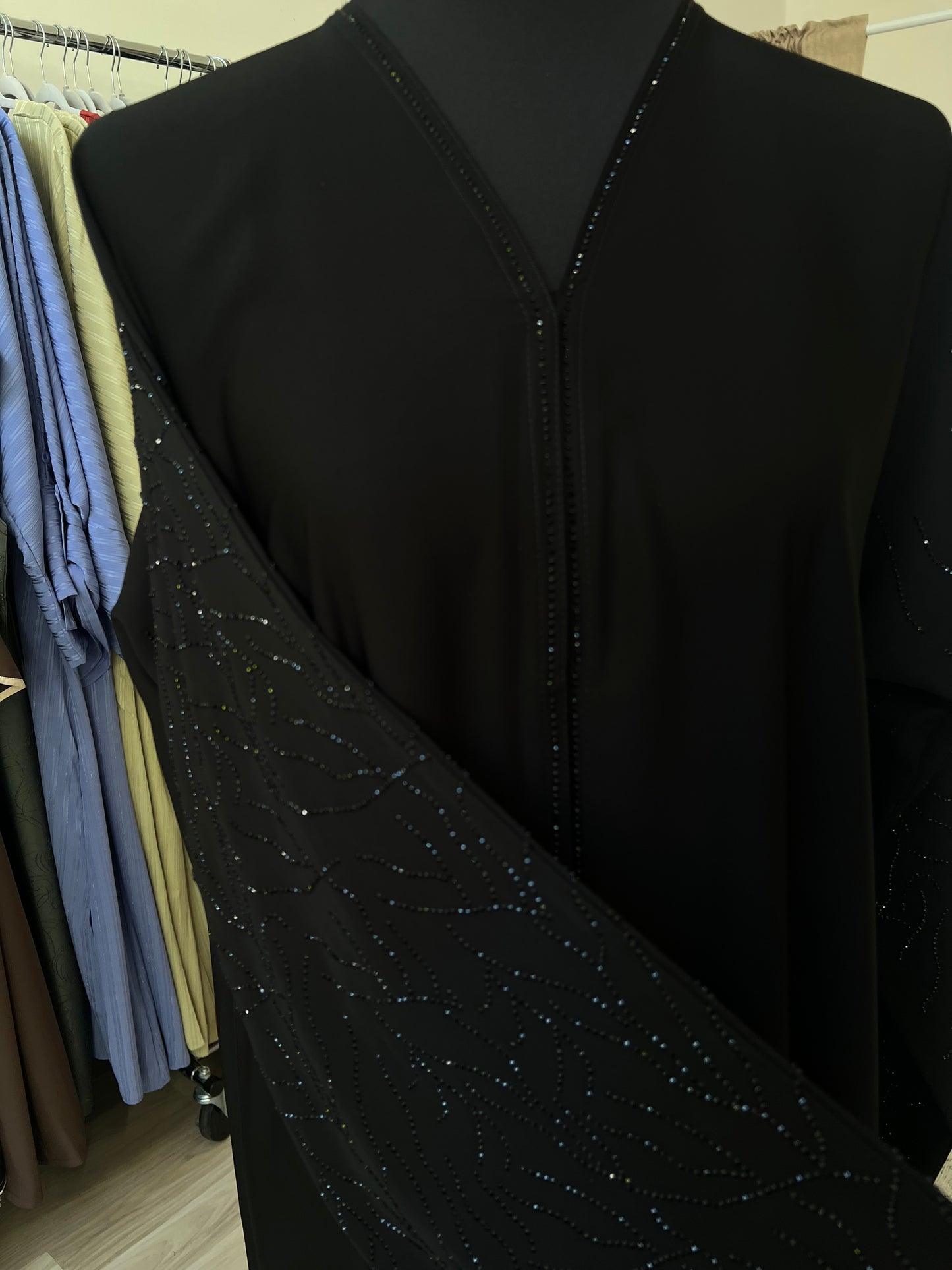 Detailaufnahme der Vorderseite der Abaya Noura mit Glitzerdetails entlang des V-Ausschnitts und am Ärmel.