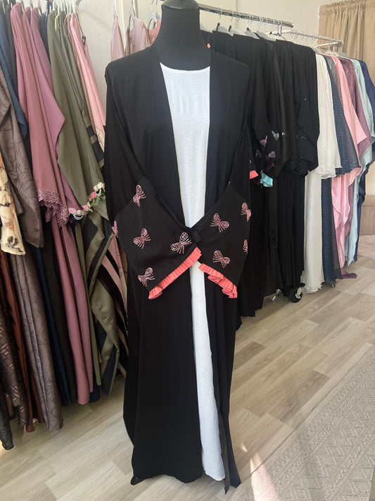 Schwarzer, offener Kimono mit rosa Schleifenstickerei und plissierten Rüschenärmeln über weißem Unterkleid – präsentiert im Sheylin Showroom.