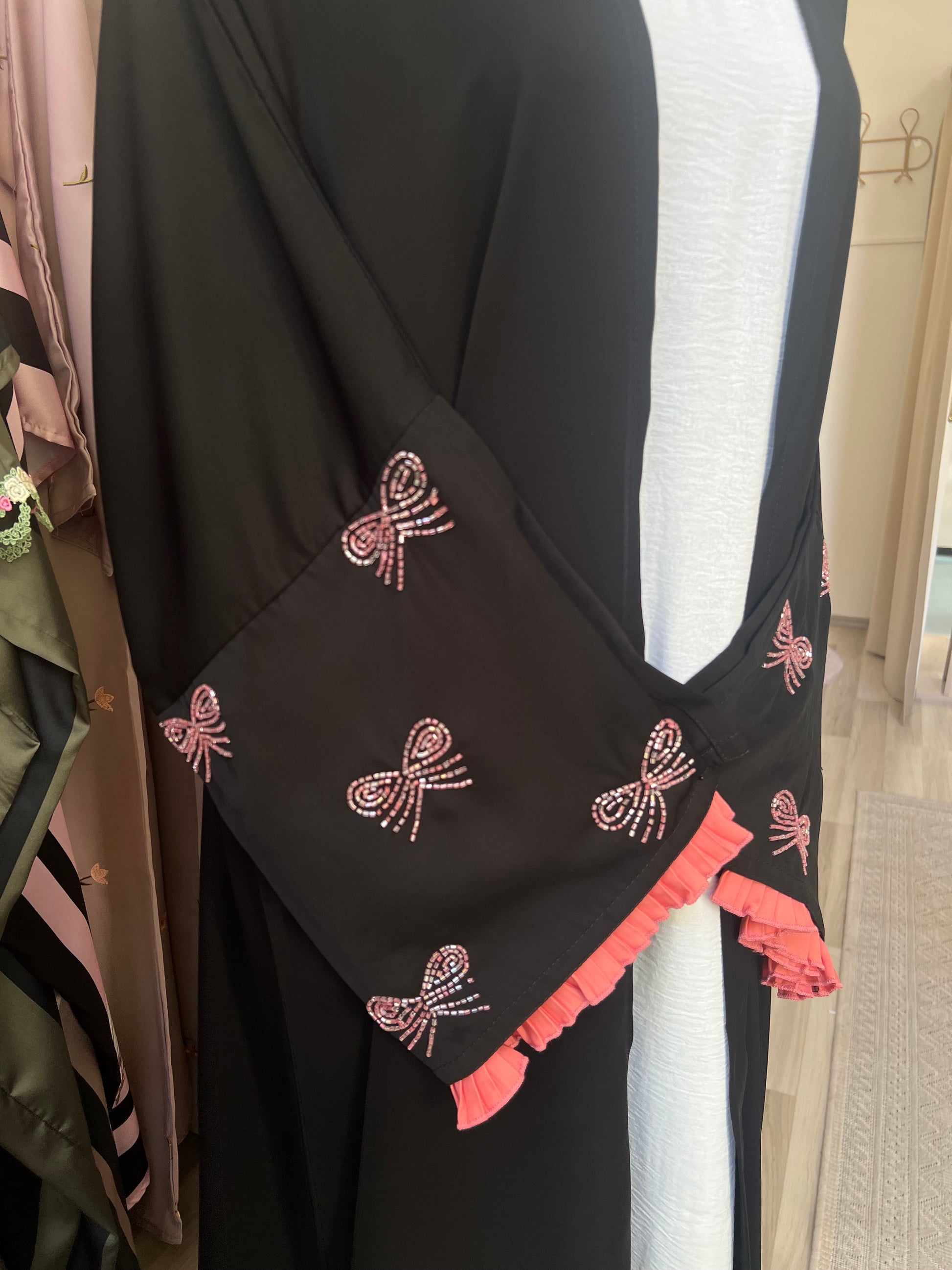 Nahaufnahme der bestickten Ärmel: rosa glitzernde Schleifenverzierungen und plissierte Rüschenkante in Pink als verspielter Akzent.
