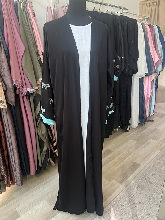 Offener schwarzer Kimono mit türkisfarbenen Rüschenärmeln und weißen Schleifenstickereien, getragen über einem weißen Unterkleid.