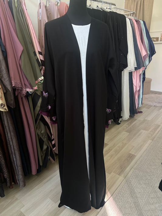 Offener schwarzer Kimono mit violetten Rüschenärmeln und Schleifenstickerei, kombiniert mit einem weißen Unterkleid – präsentiert auf einer Schneiderpuppe.
